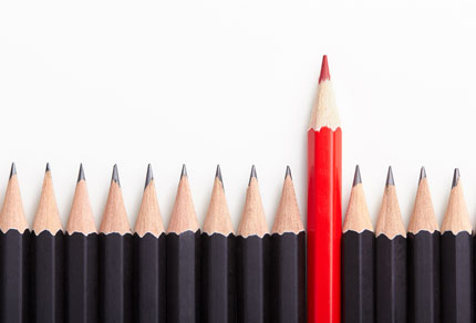 A line of black pencil crayons with one red pencil crayon standing taller.