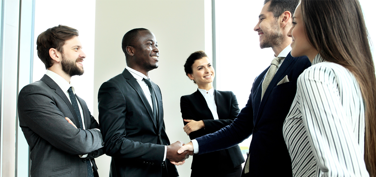 Group of business people surrounding two people shaking hands.